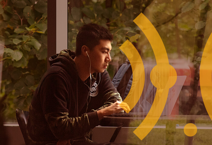 Photograph of a young man working on a computer near a window. Yellow graphics are overlaid.