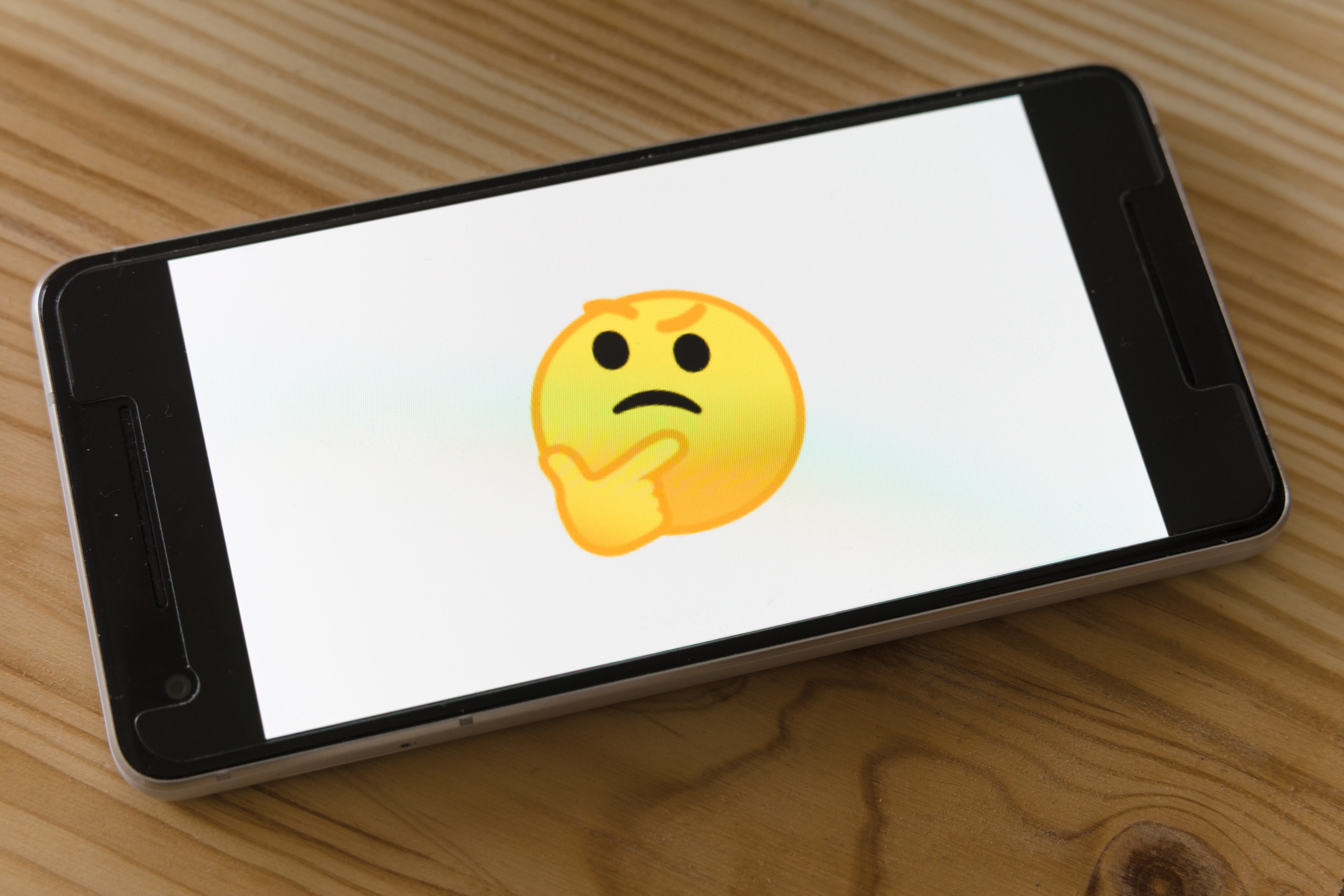 Stock image of a skeptical emoji on the screen of a smartphone