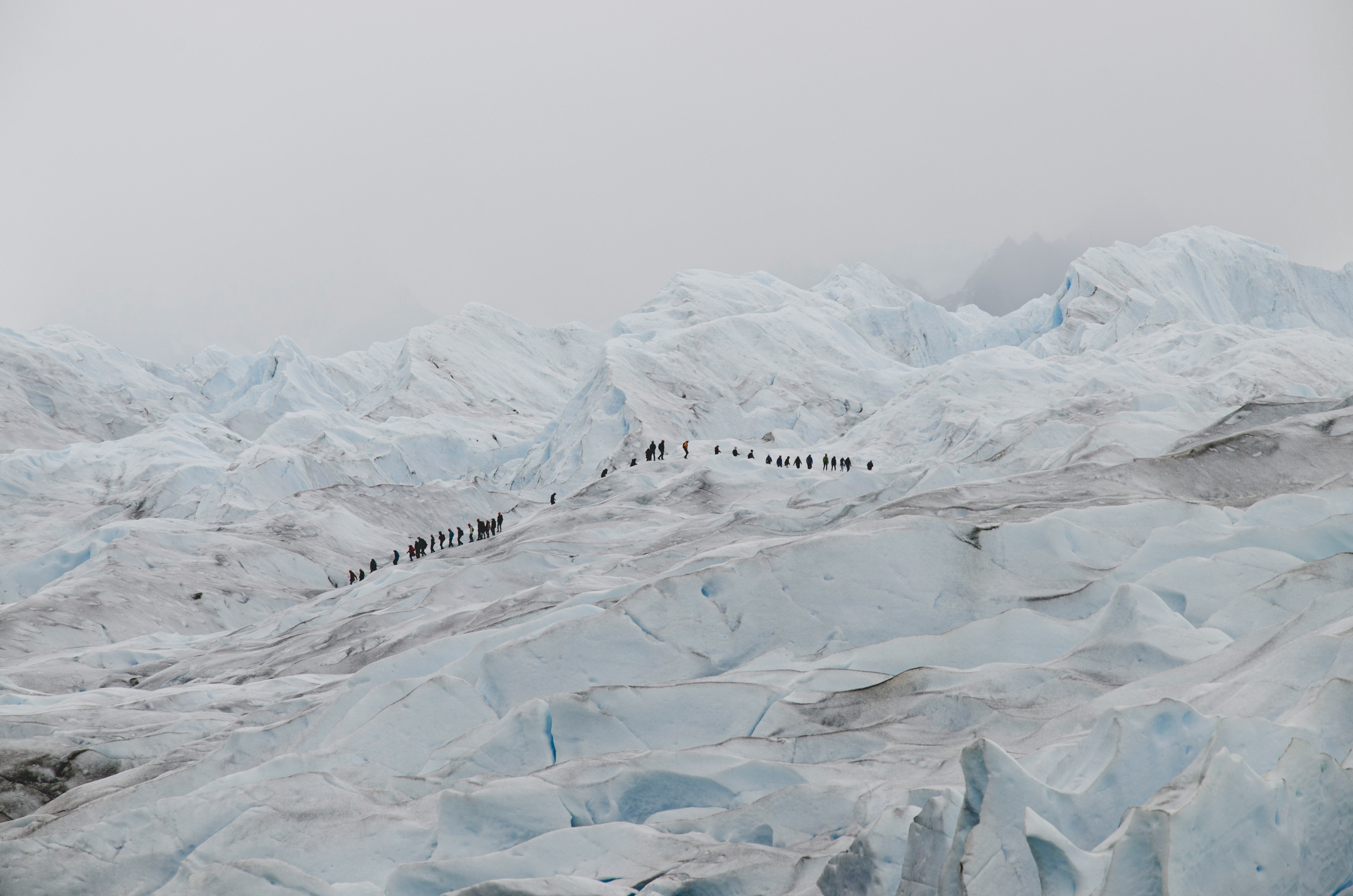 Photo of a snowy mountain range; in the distance, a line of people traversing the range can be seen